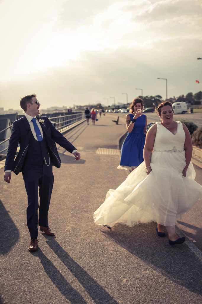 A bride and groom walking down the street after having some photos taken on a beach.