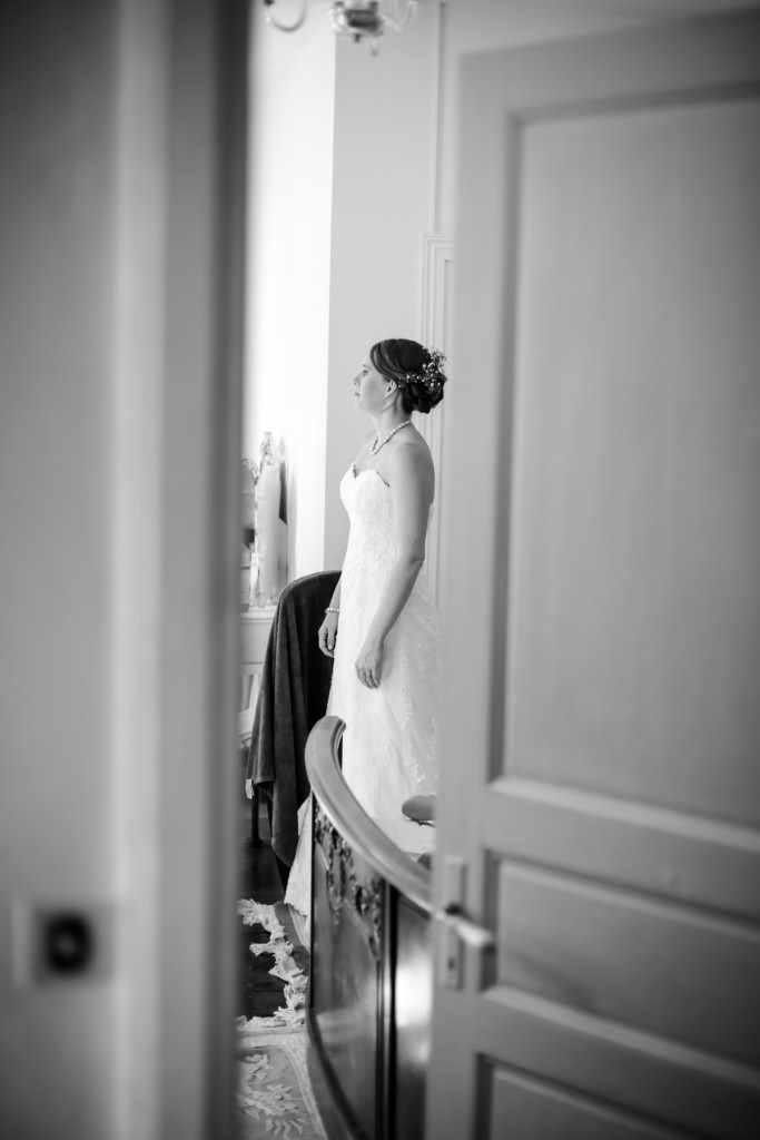 A bride looking at herself getting ready in a mirror in a french house during her wedding. Creative edit in black and white.