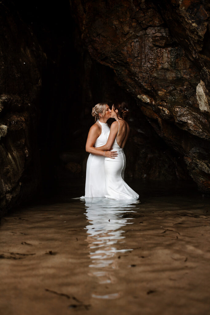 same sex wedding, two brides in a cave on a Cornish beach getting wet and kissing.