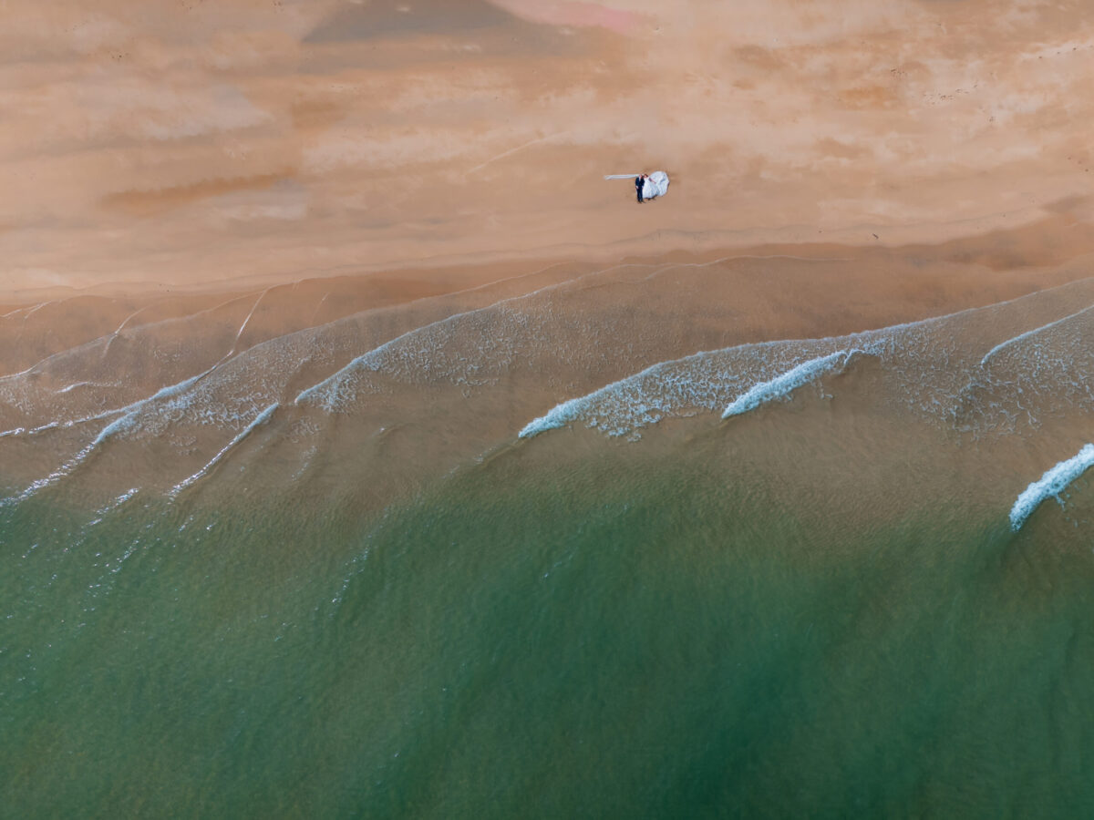 Aerial view of beach and waves. Of a married couple laying down.
