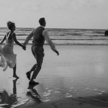 black and white image of a couple running on the beach as they elope to Cornwall.