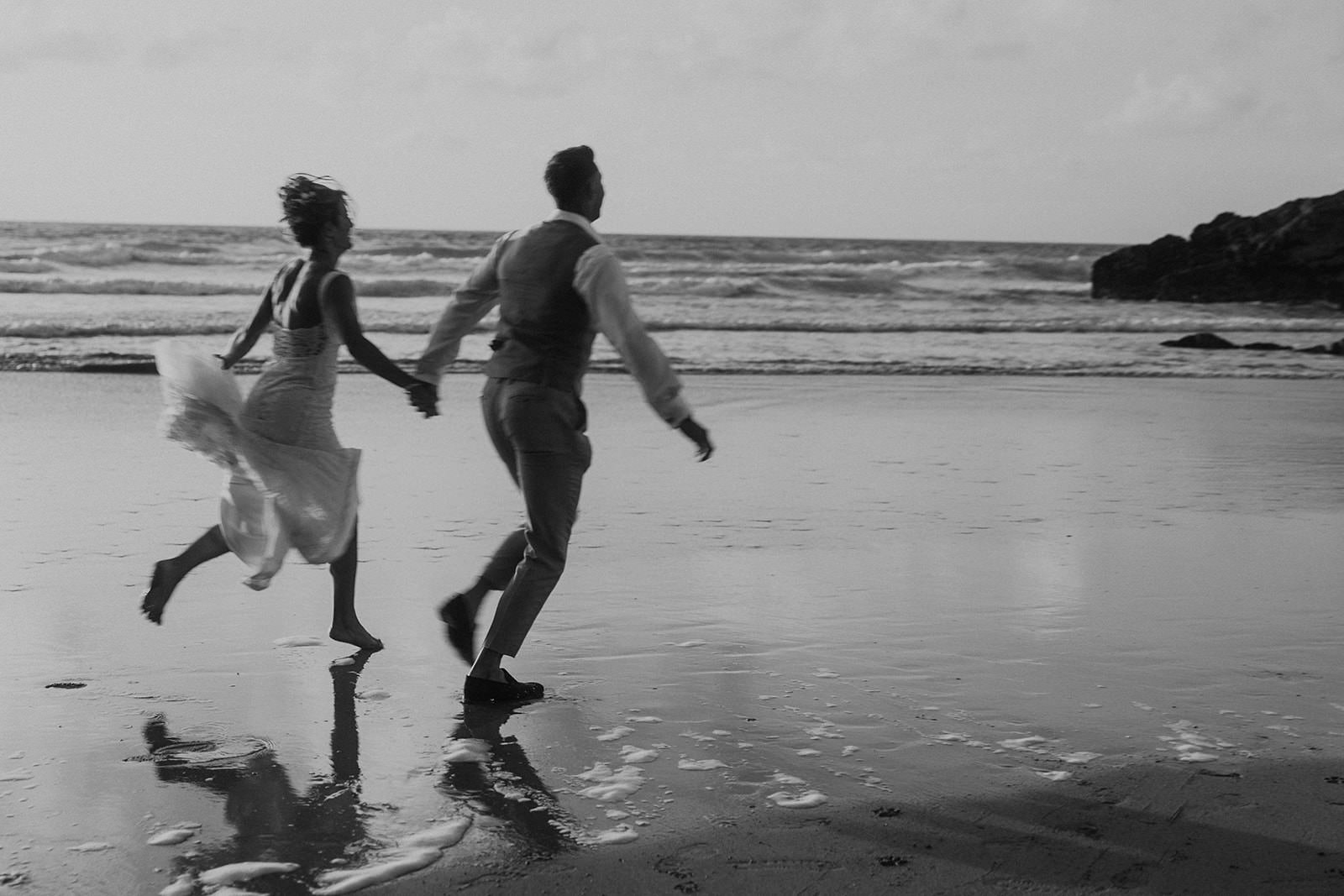 A newly married couple running together along a Cornish beach